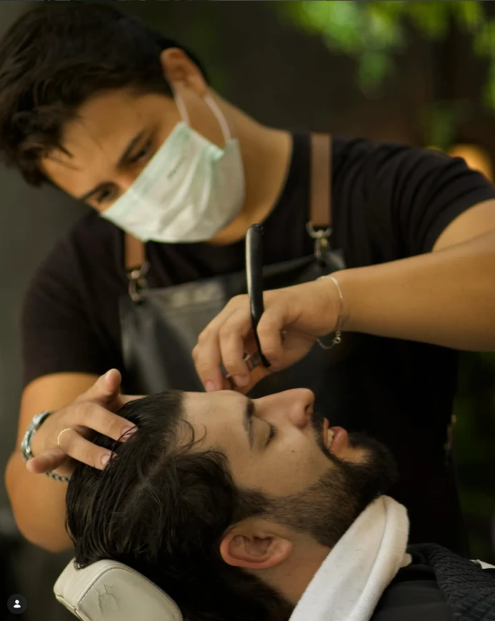 Barbeiro fazendo o acabamento da barba de um cliente com navalha